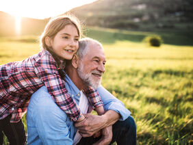 A small girl with grandfather outside in spring nature, relaxing on the grass.